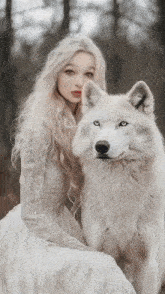 a woman in a white dress sits next to a white wolf