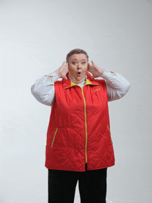 a woman wearing a red vest with a yellow zipper has her hands to her ears