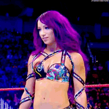 a woman with purple hair is standing in a wrestling ring wearing a colorful bra .