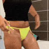a woman in a black tank top and yellow bikini bottoms is standing in a bathroom