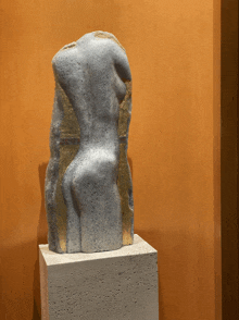 a statue of a woman 's torso is displayed on a white pedestal