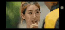 a woman is eating a candy with a toothpick in her mouth while looking at a man in a yellow jacket .