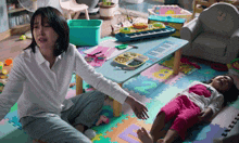 a woman sits on the floor next to a child who is laying on the floor with a keyboard in the background