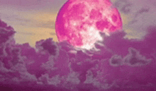 a pink full moon is shining through the clouds in the night sky .