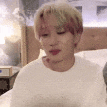 a man is sitting on a bed wearing a white sweater and looking at something .