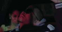 a man wearing sunglasses is laying down in a car with a woman behind him .
