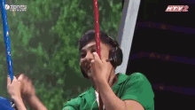a man wearing headphones and a green shirt is holding a red stick in his mouth