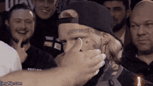 a man with a tattoo on his face is covering his face with his hand while a crowd watches .