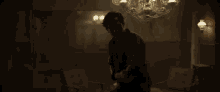 a man is standing in a dark room with a chandelier above him