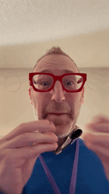 a man wearing red glasses and a blue shirt holds something in his hands