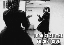 a woman in a black dress is standing in front of a mirror with the words look at all the fucks i give above her