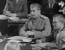 a black and white photo of a man sitting at a table with pathe written on the bottom left