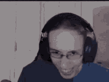 a man wearing headphones and glasses is smiling while sitting in front of a computer screen .