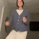 a woman is dancing in a living room wearing a blue cardigan and white pants .