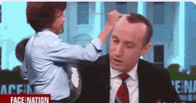 a man in a suit and tie is getting his hair done by a woman in a blue shirt .