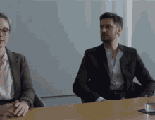 a man and a woman are sitting at a table in a meeting room .