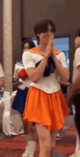 a man in a sailor suit and orange skirt is standing in a room with other people .