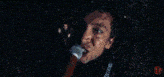 a man is singing into a red microphone with the word metallica on his jacket