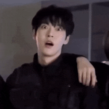 a young man is making a surprised face while standing next to another young man .