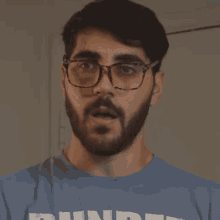 a man with a beard wearing glasses and a blue shirt that says hundred
