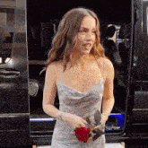 a woman in a dress is holding a red rose in front of a black van
