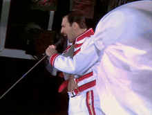 a man in a white and red uniform sings into a microphone with the letter m on his belt