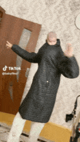 a person in a black coat is dancing with a baby on their back .