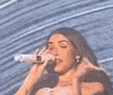 a woman is singing into a microphone in front of a blue wall .