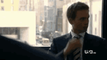 a man in a suit and tie is adjusting his tie while sitting in front of a window .