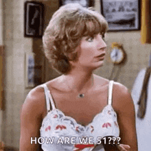 a woman in a tank top is standing in a room and talking to someone .