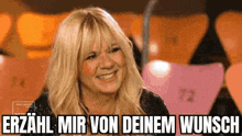 a woman is smiling in front of a sign that says erzahl mir von deinen wunsch