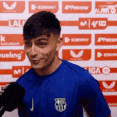 a man wearing a blue shirt with a fcb logo on it talks into a microphone