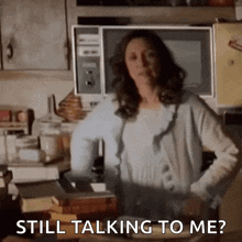 a woman is standing in a kitchen with her hands on her hips and talking to someone .