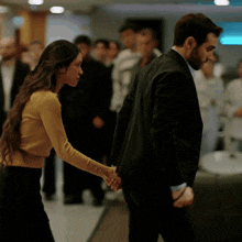a man in a suit and a woman in a yellow sweater hold hands