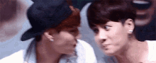 two young men are kissing each other on the cheek . one of the men is wearing a hat .