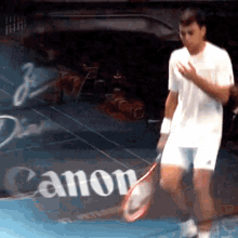 a man is holding a tennis racquet in front of a canon sign