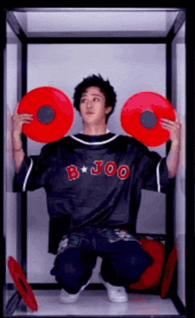 a man in a b joo shirt is holding two red circles in his hands
