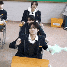 a group of young men are sitting at desks in a classroom and one of them is wearing a black jacket that says angels