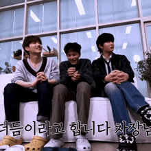 three men sit on a couch with korean writing on the bottom right