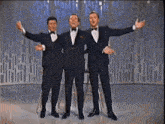 three men in tuxedos and bow ties are standing together with their arms outstretched