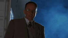 a man wearing glasses and a suit is standing in front of a window