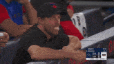 a man sitting in a dugout watching a baseball game with a scoreboard that says cle 2 tor 2