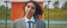 a woman wearing a suit and tie is standing in front of an orange wall .