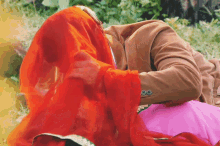 a man and woman are laying in the grass with the woman covering her face with a red veil