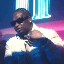 a man wearing sunglasses and a watch is dancing in front of a neon sign