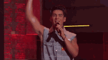a man in a denim vest is singing into a microphone .