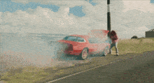 a woman stands next to a red car with the hood up