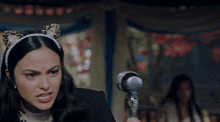 a woman wearing a cat ear headband is holding a microphone in her hand .