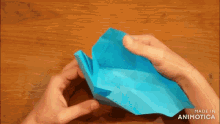 a person is holding a piece of blue paper on a wooden table made in animatica