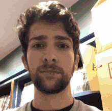 a man with a beard is standing in front of a bookshelf with the letter a visible on it